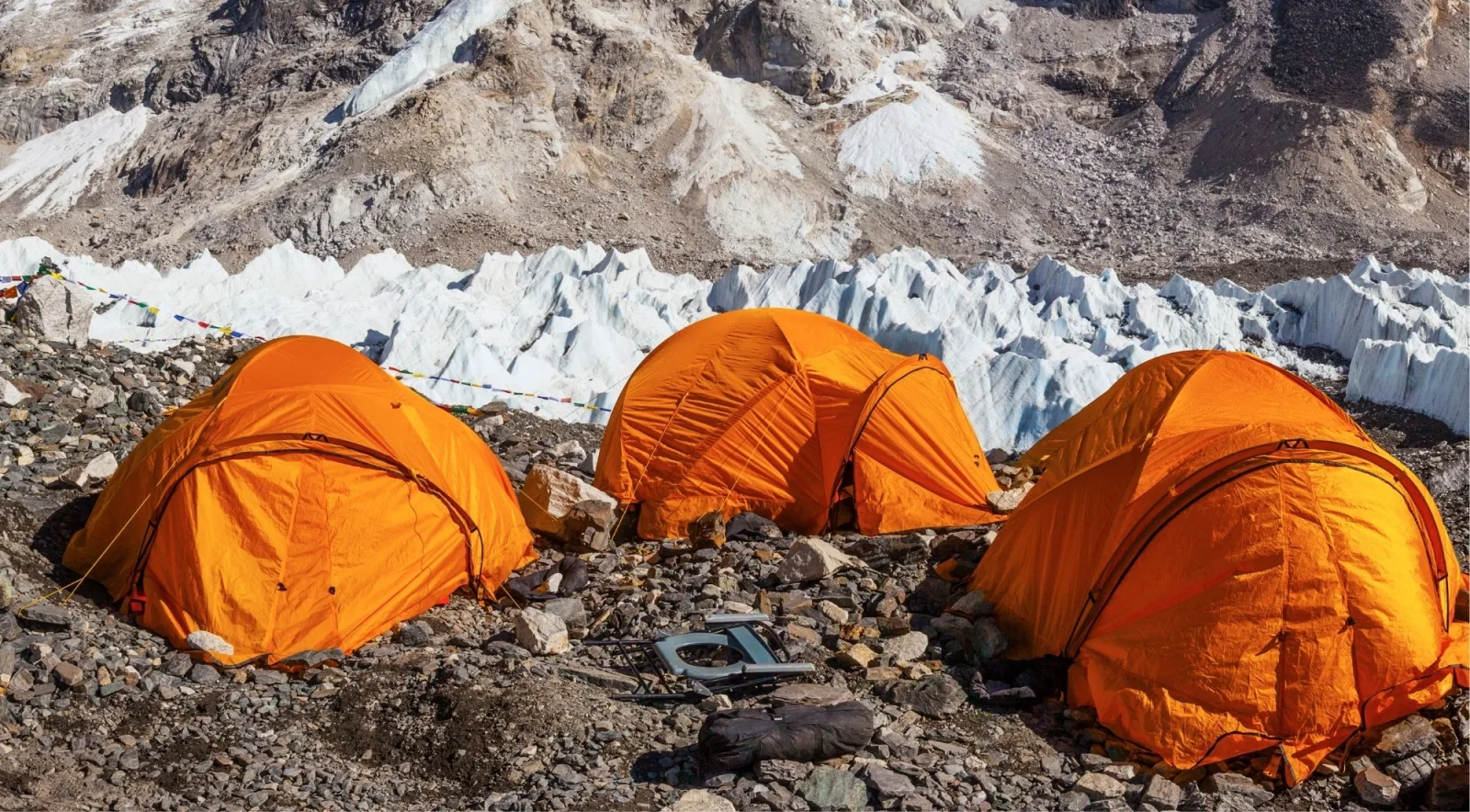 Orange expedition tents pitched on rocky ground beside the Khumbu Glacier at Everest Base Camp
