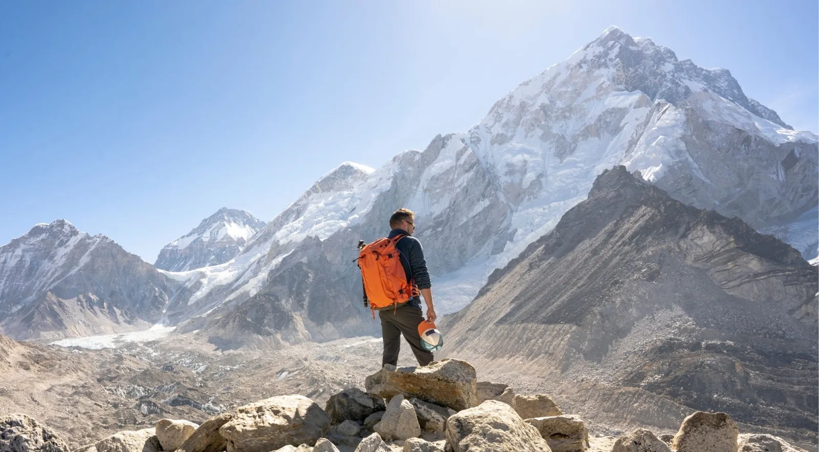Trekker with an orange backpack looking out over the Khumbu peaks