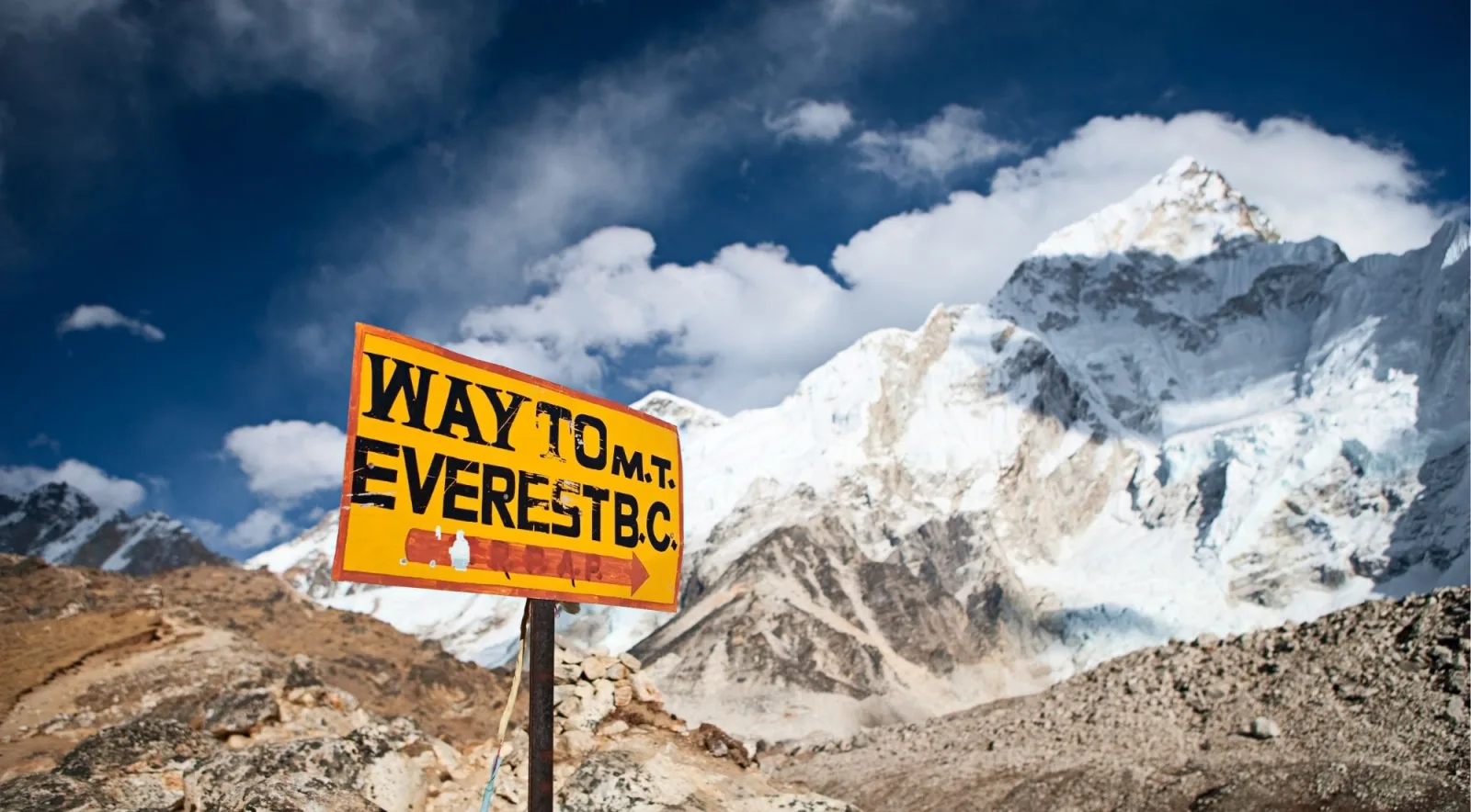 Hand-painted yellow signpost reading Way to Mt Everest B.C. with a snow peak behind