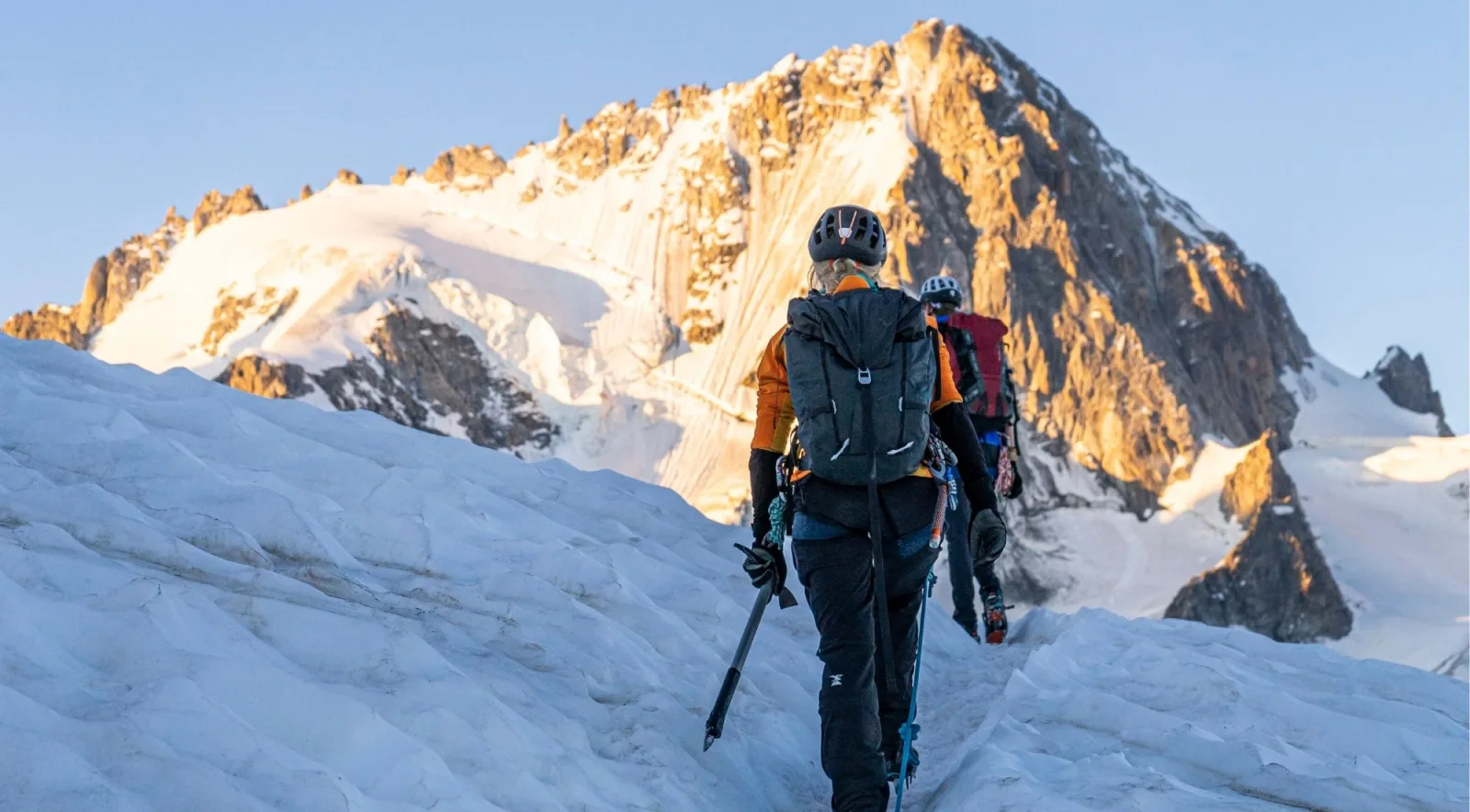 A roped mountaineering team crossing a snow ridge at sunrise