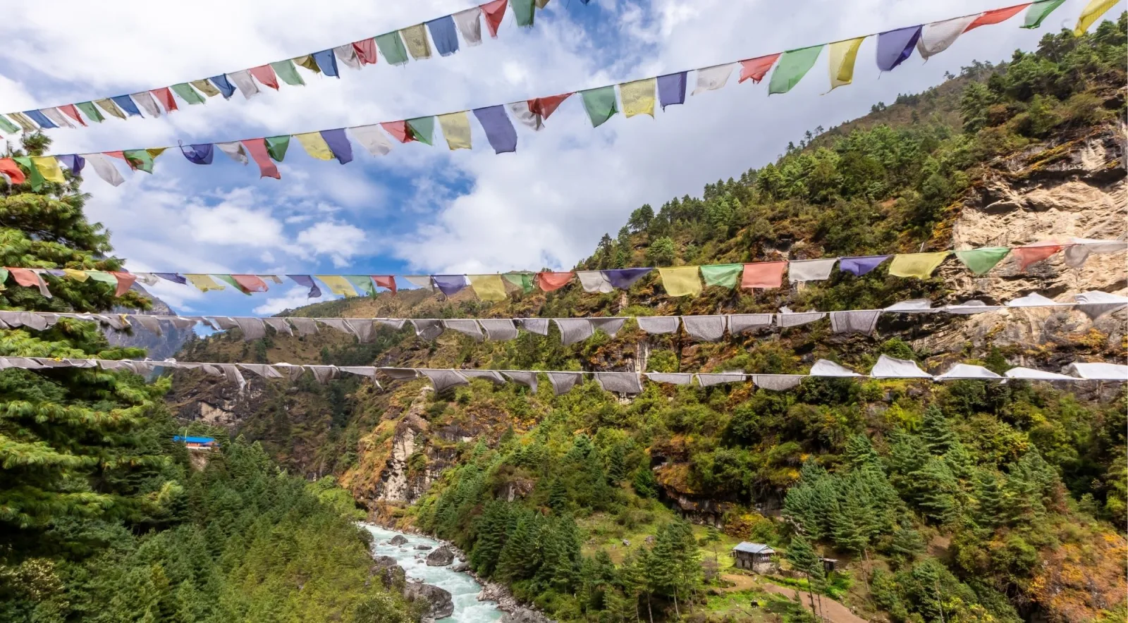 Colorful Buddhist prayer flags strung across a forested canyon above the Dudh Koshi river
